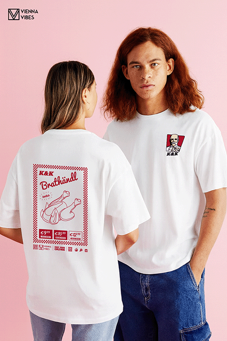 Zwei Personen tragen weiße T-Shirts mit dem „K&K“-Design aus der Fast-Food-Culture-Kollektion von Vienna Vibes. Der Mann zeigt das Brustlogo: ein Kaiser Franz Josef im KFC-Stil mit dem Schriftzug „K&K“. Die Frau präsentiert den großflächigen Rückendruck mit einem stilisierten Brathendl und rot-weißem Design – eine humorvolle Hommage an österreichische Esskultur. Beide stehen vor einem pastellrosa Hintergrund, die Shirts sind weiß mit Retro-Food-Motiven.